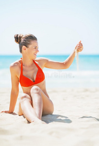 快乐的年轻女子坐在沙滩上玩沙子