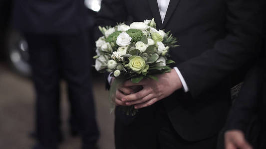 西装场合英俊的商人手捧花.新郎在一套西装,拿着一束鲜花.婚礼胸花.