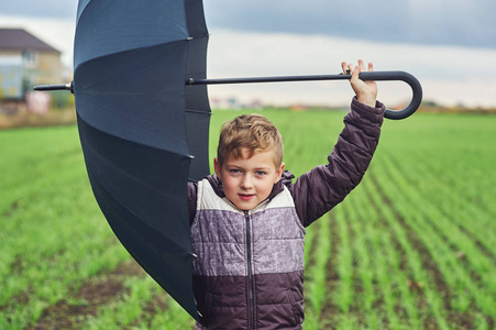 男孩秋天在田野里带着雨伞散步