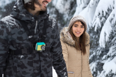 年轻浪漫的情侣漫步在雪林户外混合种族男女牵手