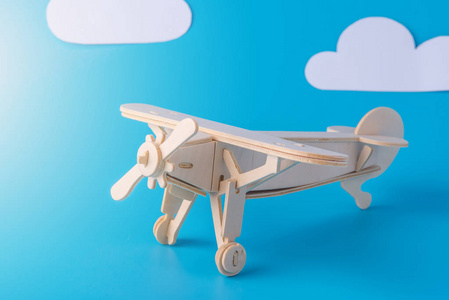 木制玩具飞机在蓝天的背景下用纸云。概念旅行和航空公司