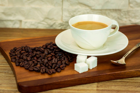 在木桌和白色砖墙背景上的糖和咖啡豆的白色杯咖啡的博览会