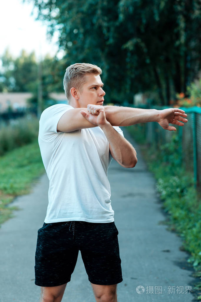 男运动员在自然热身, 街道在城市, 热身的手的肌肉.在夏天在公园.