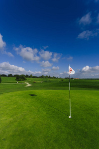 一个绿色的高尔夫球场, 洞和旗帜的明亮的阳光明媚的一天的看法。运动, 放松, 休闲和休闲的概念。阳光下的夏日风景