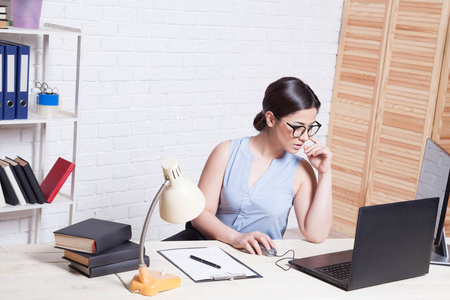 业务在眼镜的女孩坐在办公室在电脑文件夹纸