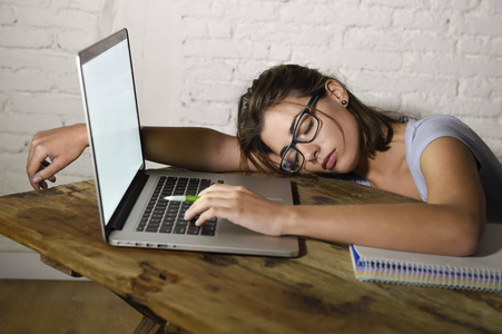 年轻美丽和疲倦的学生女孩睡觉小睡躺在家里笔记本电脑办公桌疲惫和浪费的花费晚上学习