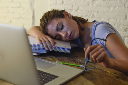 年轻美丽和疲倦的学生女孩睡觉小睡躺在家里笔记本电脑办公桌疲惫和浪费的花费晚上学习
