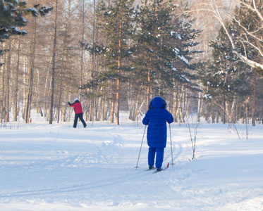 一位年长的妇女在冰雪覆盖的冬季森林或公园里滑雪, 退休后的积极生活方式