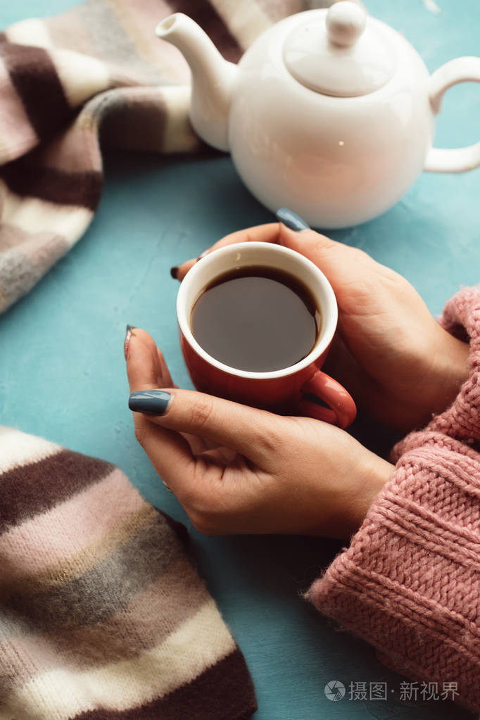 女人在蓝色的背景下捧着一杯热茶