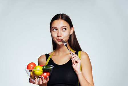 一个美丽的年轻女孩在一个黑色的顶部想要减肥, 拿着一个盘子, 有用的蔬菜和水果