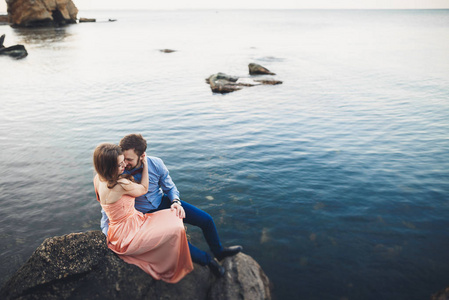 新婚夫妇坐在蓝色的海附近的大石头上