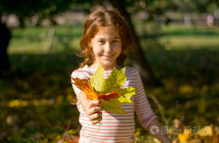 一个 redhaired 的女孩在秋天手里拿着黄叶子