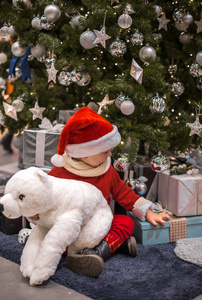 小圣诞老人和泰迪熊坐在圣诞树旁边