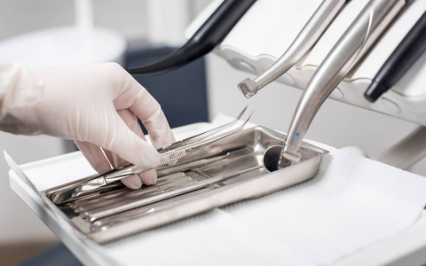 牙医用戴手套的手在牙科诊所里采摘牙科镊子。关闭, 选择性焦点。牙科
