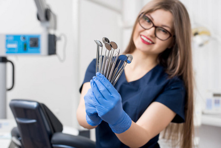 微笑女牙医与蓝色手套藏品工具牙科镜子和牙科探针在牙医室。特写, 有选择地关注工具。牙科