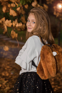可爱的小女孩穿着大衣和靴子坐在秋天的背景, 金色的秋叶