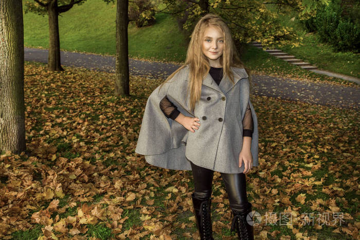 可爱的小女孩穿着大衣和靴子坐在秋天的背景, 金色的秋叶