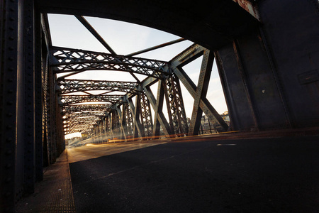 在一个阳光明媚的日子里, 沥青路在一座城市桥的钢结构下。桥梁隧道中的城市场景。长时间曝光。色调