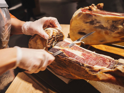 一个女人的手在市场或商店的手套削减了传统的西班牙 jamon de bellota。肉类关闭