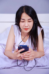 女人在耳机听音乐从智能手机在床上