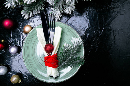 圣诞餐桌地点设置。假日背景。绿色的盘子刀叉和圣诞装饰品在黑桌上。顶部视图