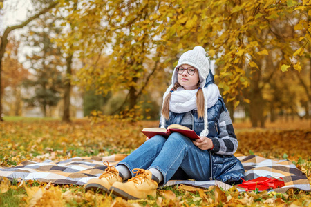 一个寒冷的公园里的少女学习一本书, 坐在一个冰冷的地面上的毯子