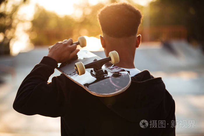 一个男十几岁的男子持有滑板的背面视图