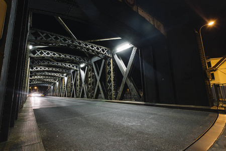 在城市的一座桥梁的钢建筑下的沥青路。夜晚的城市景象, 在隧道中有汽车灯的踪迹。调子