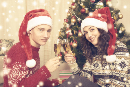幸福的夫妇与圣诞树和一杯香槟在家里。寒假和爱情的概念。黄色色调与雪