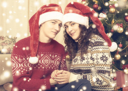 幸福的夫妇与圣诞树和装饰在家里。寒假和爱情的概念。黄色色调与雪