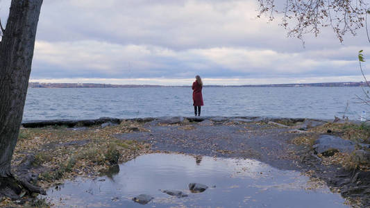 在一个湖和秋天树的背景下, 一个穿着红色大衣的女孩的后视图.