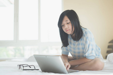 可爱的亚洲女孩坐在床上，在白色床上使用笔记本电脑