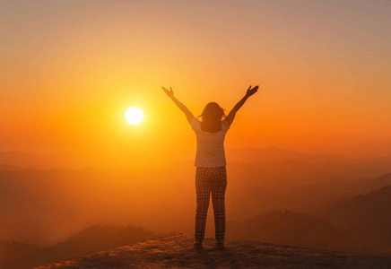 silhoutte 年轻的亚洲妇女站起来举起双臂在日落时高高的悬崖上欣赏