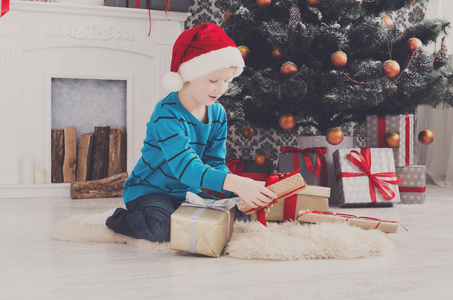 可爱的男孩，在圣诞老人的帽子展开圣诞礼物