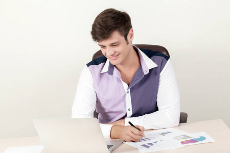 年轻的商人坐在办公室里和在新项目上工作时使用他的笔记本电脑的肖像