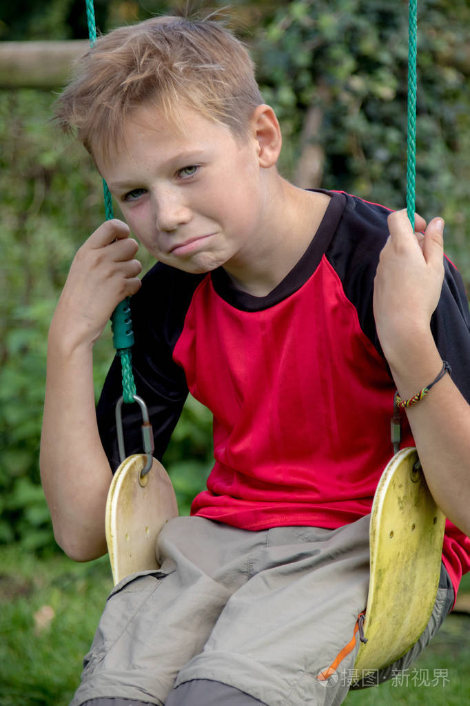 悲伤的英国男孩坐在秋千上