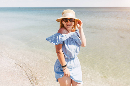 美丽的年轻快乐女人的肖像，戴着草帽，穿着蓝色的裙子，背景是大海