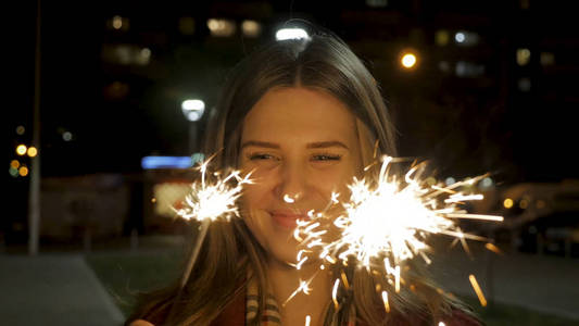 美丽的微笑年轻女子捧着烟火。夜景。年轻的微笑着的女孩，她手里拿着烟火。节日概念