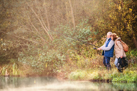 高级夫妇秋天在湖边钓鱼。