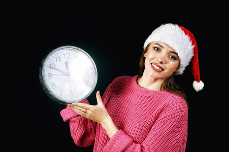 年轻妇女在圣诞老人帽子藏品时钟