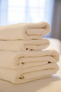 一叠毛巾放在酒店房间的床上，背景是窗户