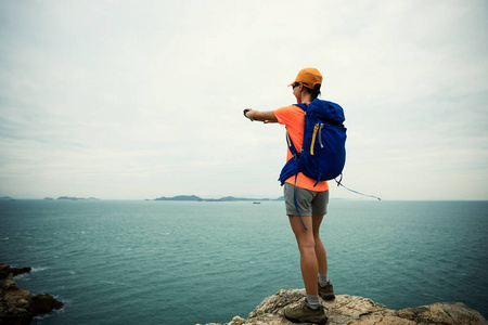 海边悬崖上使用智能手机的年轻女子徒步旅行者