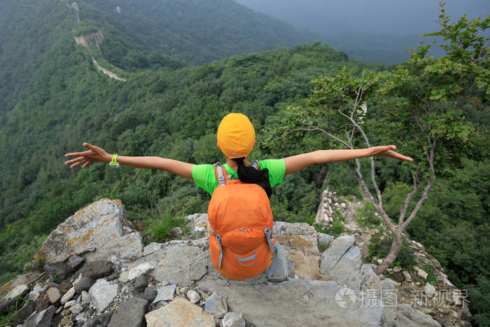 成功的年轻女子徒步旅行者张开双臂站在长城上