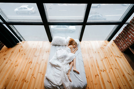 年轻苗条的美丽的赤脚女孩躺在白色舒适的床上, 毯子和枕头和睡觉.