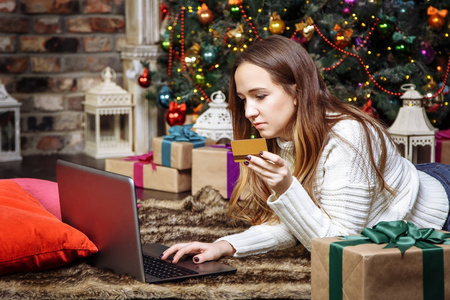 年轻的妇女做网上购物与信用卡和笔记本电脑在家里。圣诞购物理念