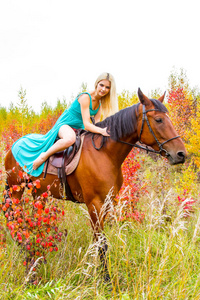金发美女骑一匹马走在秋天的森林