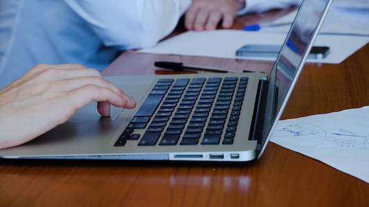 年轻的职业商人穿着黑色的高领毛衣, 用现代笔记本电脑, 在笔记本电脑上打字的男性手特写