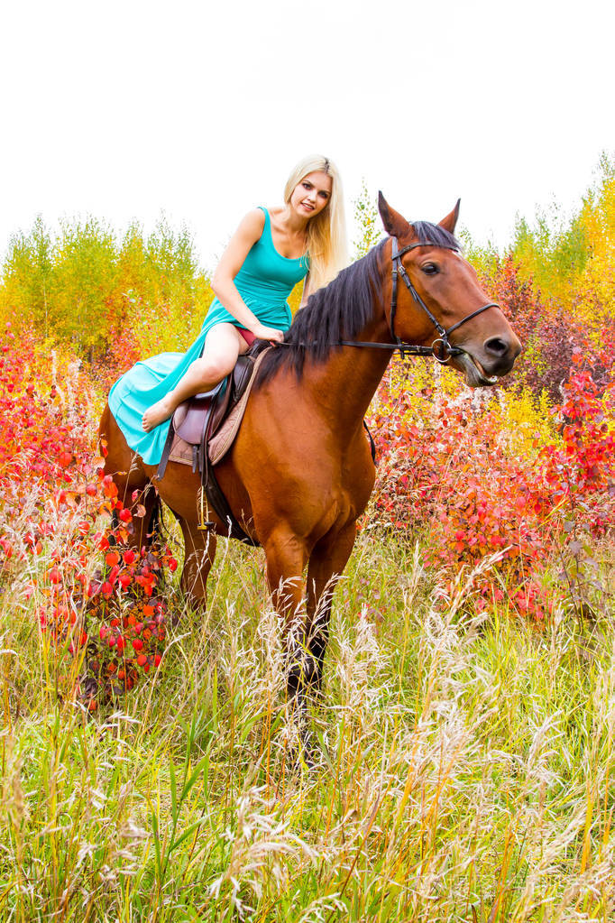 金发美女骑一匹马走在秋天的森林