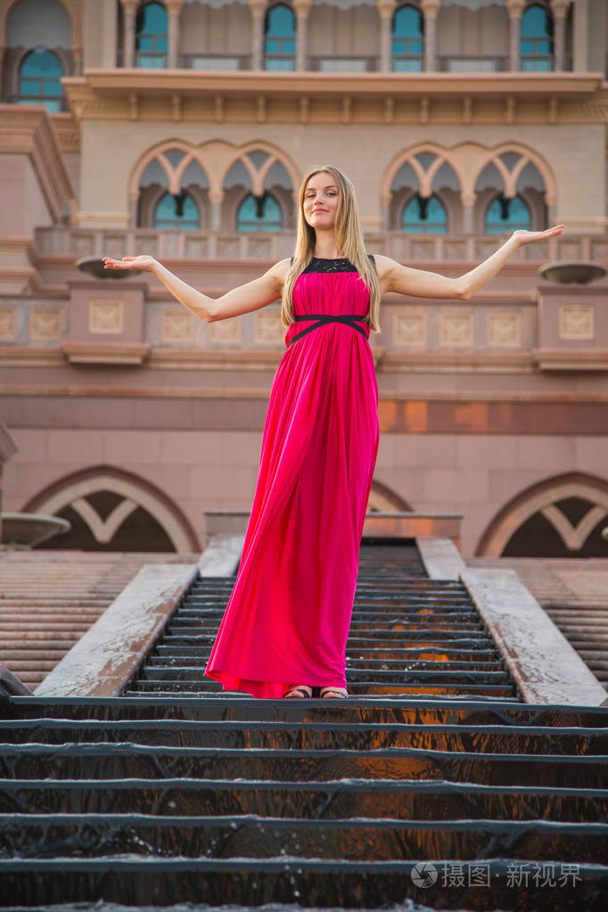 年轻的美女著名的女人穿着飘扬的红色连衣裙在阿布扎比酋长国宫附近的
