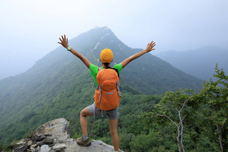 年轻女子徒步旅行者张开双臂来到山顶的长城